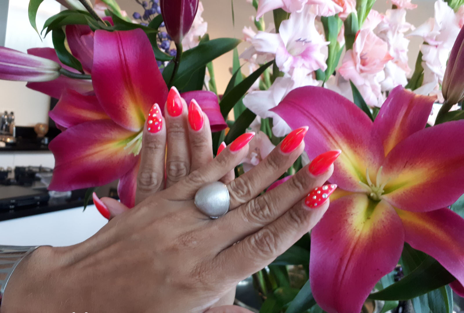 Rode nagels met witte stippen tussen lelies